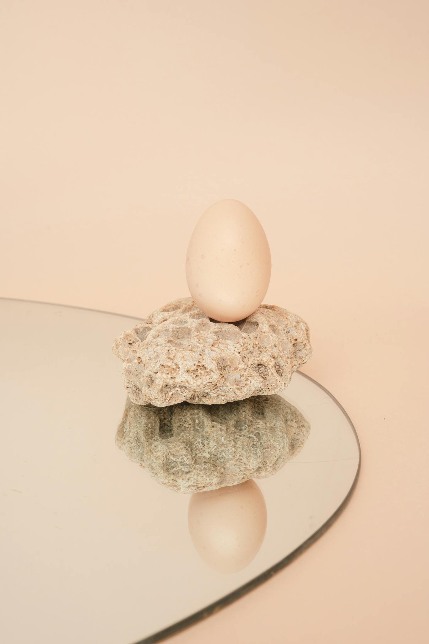 A single egg placed on stone with a mirror reflection, showcasing minimalist design and pastel tones.