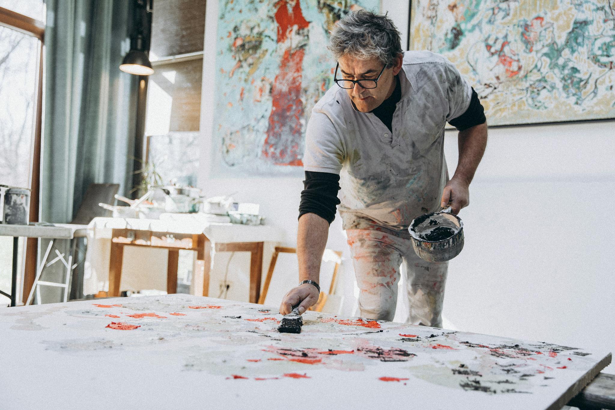 Adult male artist creating abstract artwork in a well-lit studio space, working passionately on a large canvas.